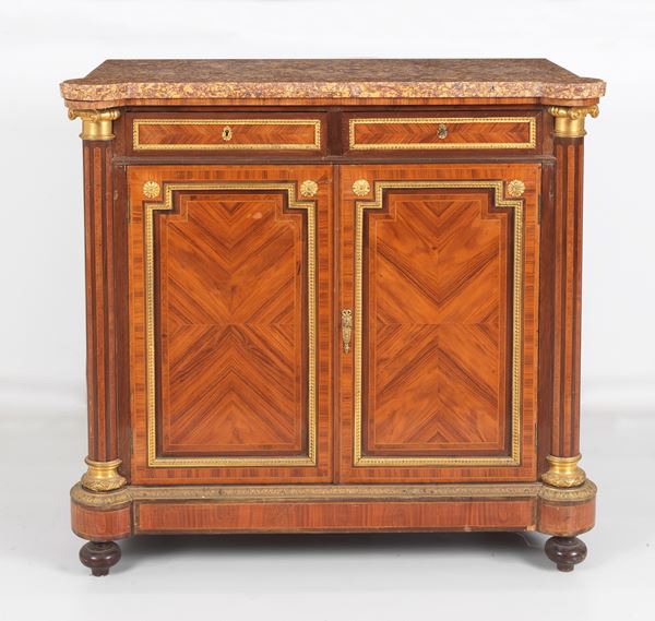 Antica credenza francese Napoleone III in ebano viola, bois de rose e mogano, con filettature intarsiate e guarnizioni e fregi in bronzo dorato, sbalzato e cesellato, montanti a colonnine neoclassiche scannellate, due tiretti con due sportelli sottostanti e gambe a cipolla. Piano in marmo brecciato