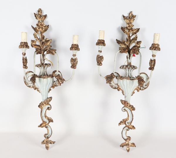 Coppia di appliques in legno dorato e laccato avorio, intagliate a motivi di anfore con fiori, 2 luci ciascuna. Lieve difetto