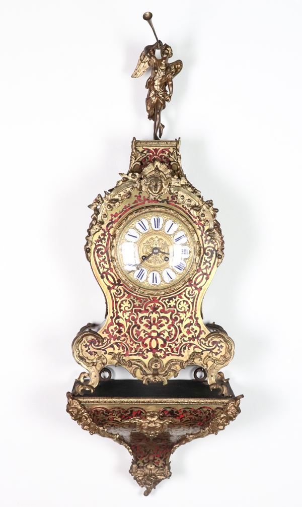 Antico orologio a cartel francese da parete con mensola, di linea Luigi XV, con intarsi alla maniera Boulle in metallo dorato su fondo rosso, guarnizioni e sculture in bronzo dorato e cesellato, sormontato da scultura di "Angelo con tromba". Quadrante con cifre romane in smalto bianco e blu. Macchinario firmato all'interno, non funzionante, da revisionare