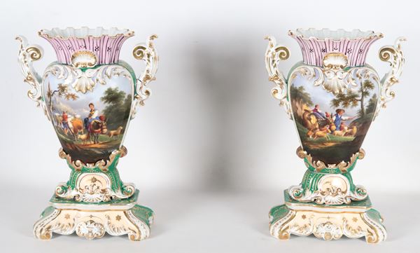 Coppia di antichi vasi napoletani a cartoccio Epoca Luigi Filippo, in porcellana policroma interamente decorati con "Scene pastorali e medaglioni con mazzi di fiori", lumeggiature in oro zecchino. Un vaso presenta lieve sbeccatura al bordo del collo e nell'altro vaso una parte del manico è rincollata