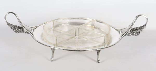 Antica antipastiera a forma tonda in metallo argentato, sbalzato e cesellato con due manici ricurvi e sorretta da quattro piedini, quattro vaschette in cristallo