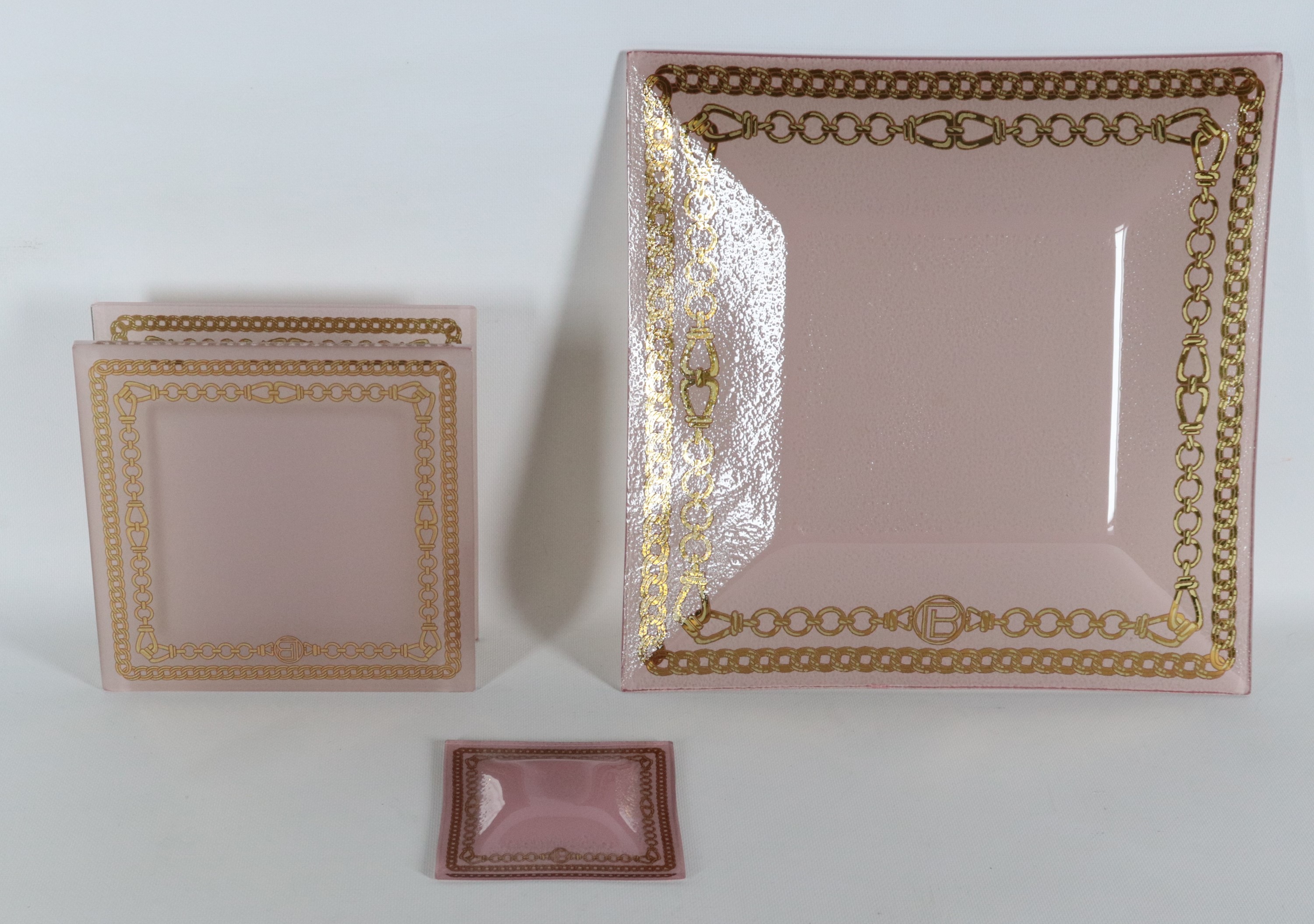 Lotto di tre originali centrotavola in vetro rosa con bordi dorati a motivi di cordoni intrecciat...