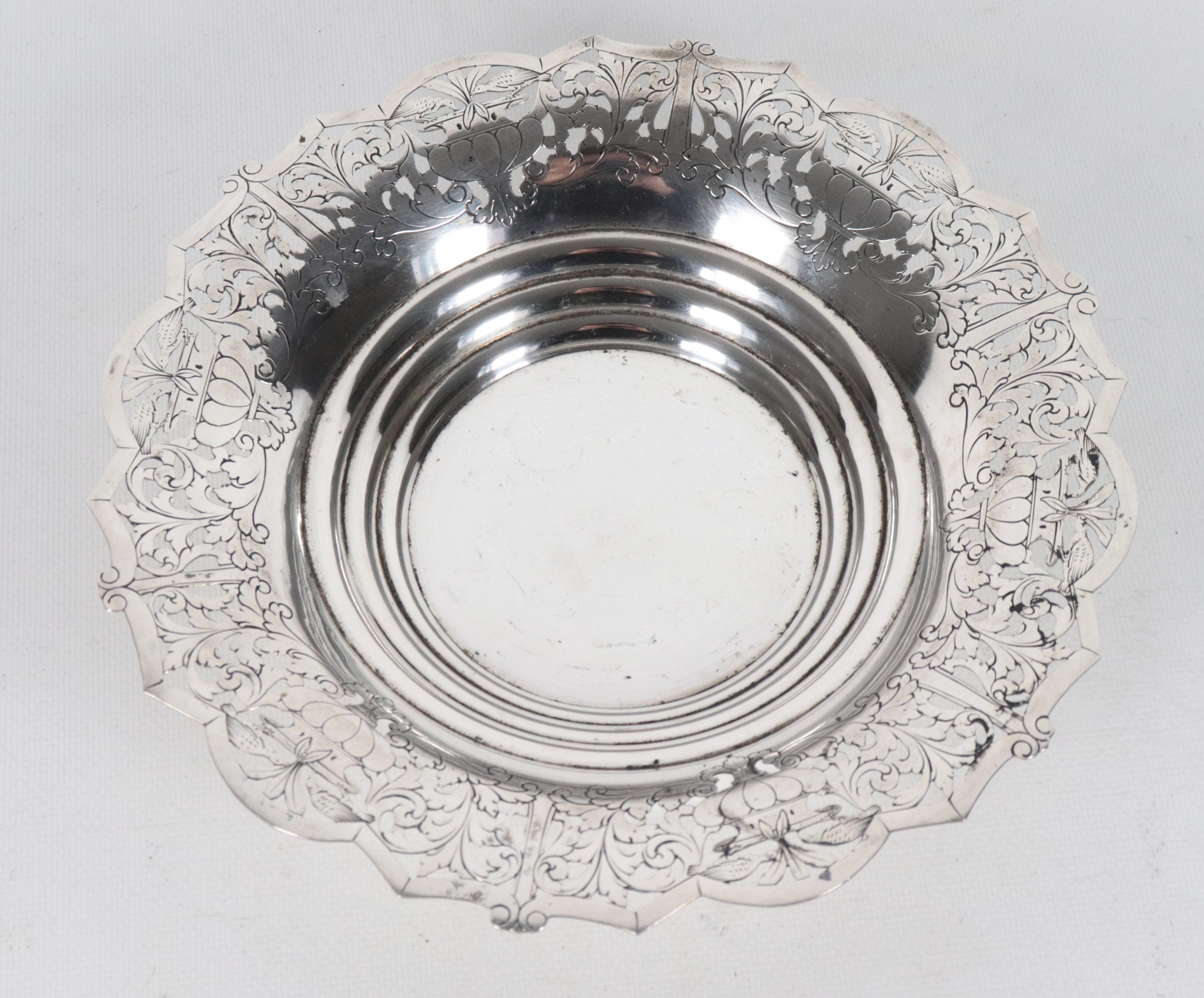 Centrotavola tondo in argento con bordo sagomato, cesellato e traforato a motivi di volute florea...
