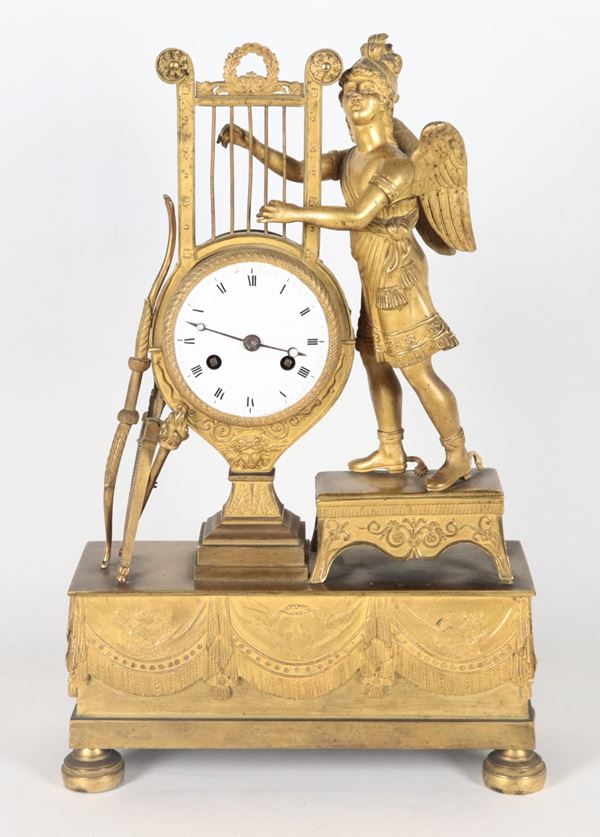 Antique French Empire period table clock, in gilded bronze, embossed and chiseled with a sculpture of a winged soldier with a lyre, bow, and quiver. White enamel dial.