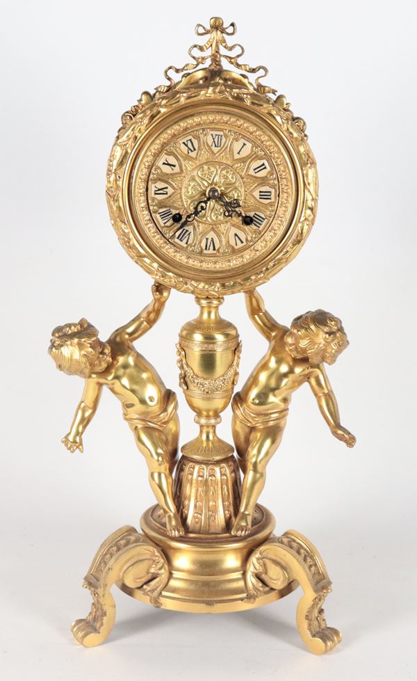 French table clock in gilded bronze, chiseled and embossed with Louis XVI motifs, dial supported by sculptures of cherubs with amphora