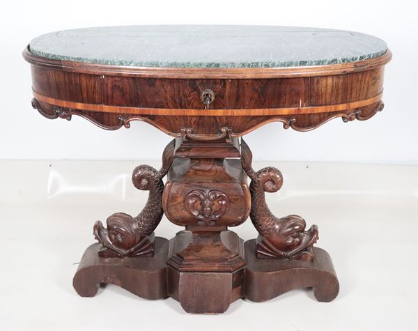 Antique Neapolitan Louis Philippe walnut center table, oval in shape with a base made up of carved dolphin sculptures, a central drawer and a marble top