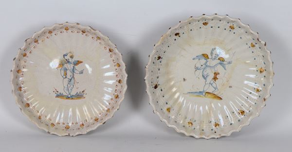 Lot of two antique glazed Faenza majolica crespines, with polychrome decorations featuring cupid motifs and floral garlands