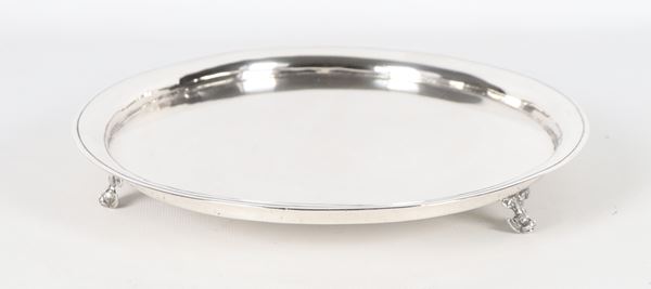Round silver metal salver, supported by three curved feet