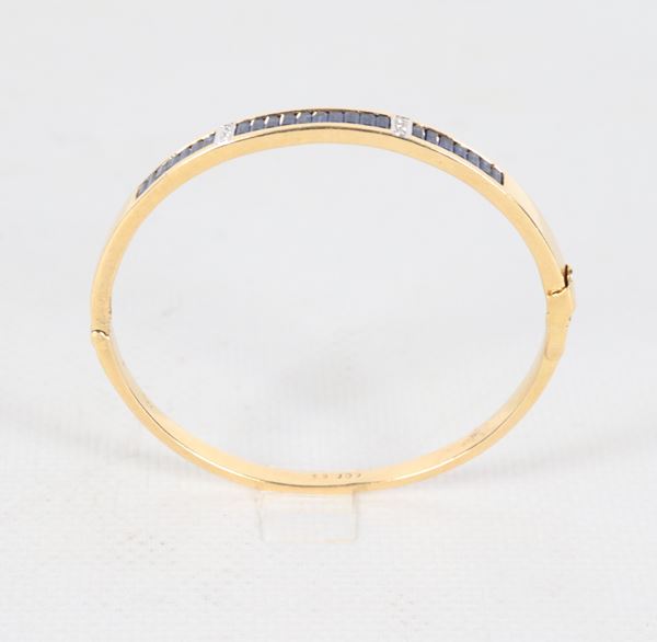 Bracciale a manetta in oro giallo 18kt, con piccoli diamanti ct 0,06 circa e zaffiri taglio carrè. Peso lordo gr. 20,5