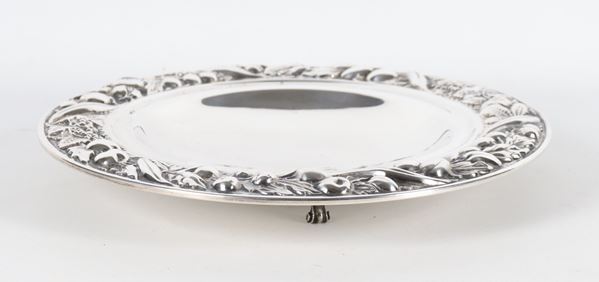 Fruttiera tonda in argento, con bordo cesellato e sbalzato a volute e intrecci di frutta, sorretta da tre piedini ricurvi, gr. 630