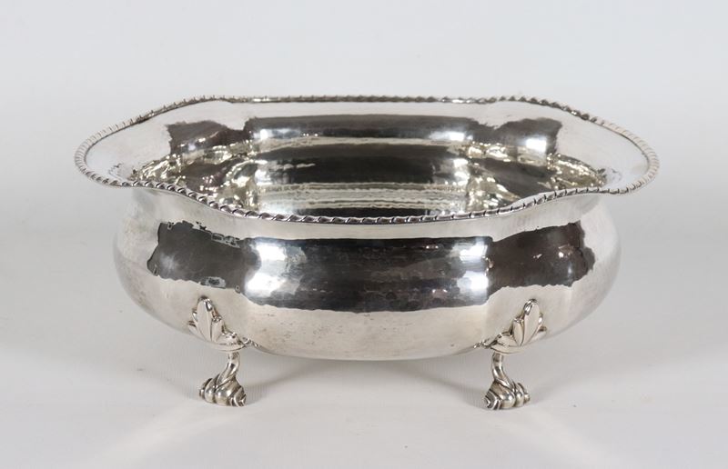 Fruttiera ovale in argento con bordo centinato, cesellato e sbalzato, sorretta da quattro piedini...