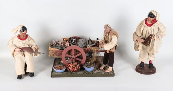 "Due pulcinella suonatori e venditore di pesce con carretto", lotto di tre pupazzi del presepe napoletano in terracotta e tessuto