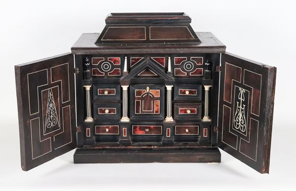 Antico monetiere da tavolo in legno ebanizzato con due piccoli sportelli, all'interno intarsi, colonnine e tiretti. La parte superiore apribile con segreto scorrevole 