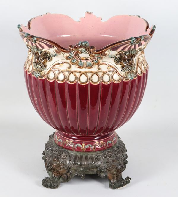 Cachepot Liberty in ceramica porcellanata e smaltata color sangue di bue, con decorazioni a rilievo di volute floreali, intrecci e mascheroni. Base in bronzo sbalzato