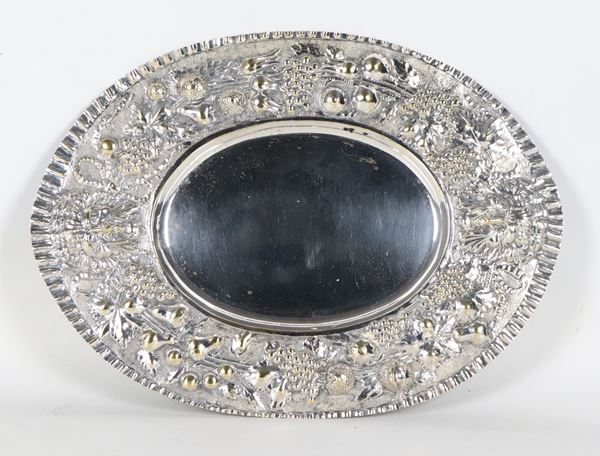 Piatto ovale in metallo argentato, con bordo cesellato e sbalzato a motivi di grappoli d'uva e mascheroni