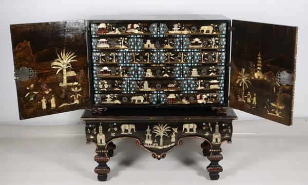 Antico e raro cabinet monetiere orientale a due corpi. La parte superiore a due sportelli con tiretti all'interno interamente decorati con argento filigranato, turchesi, giade, pietre dure e madreperla a motivi di templi, pagode, animali e arabeschi. La parte sottostante con basamento a consolle con ricche decorazioni a rilievo a motivi di pagode, fiori, palme ed elefanti                                                   