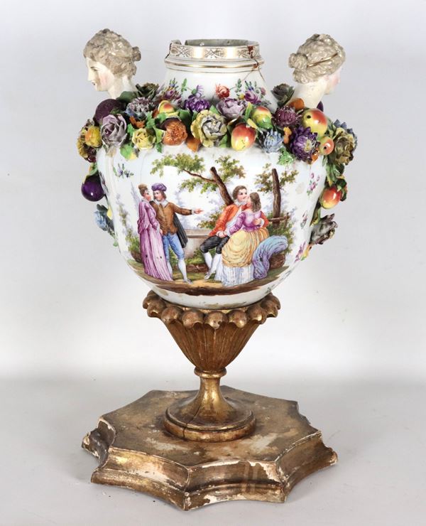 Antico vaso in porcellana di Sassonia con sculture e ghirlande di fiori e frutta a rilievo e "Scene galanti" dipinte, sorretto da base in legno dorato e intagliato
