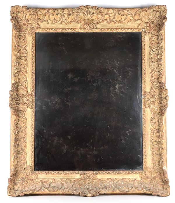 Antique gilded wooden frame carved with plant scrolls and shells, with a mercury mirror inside