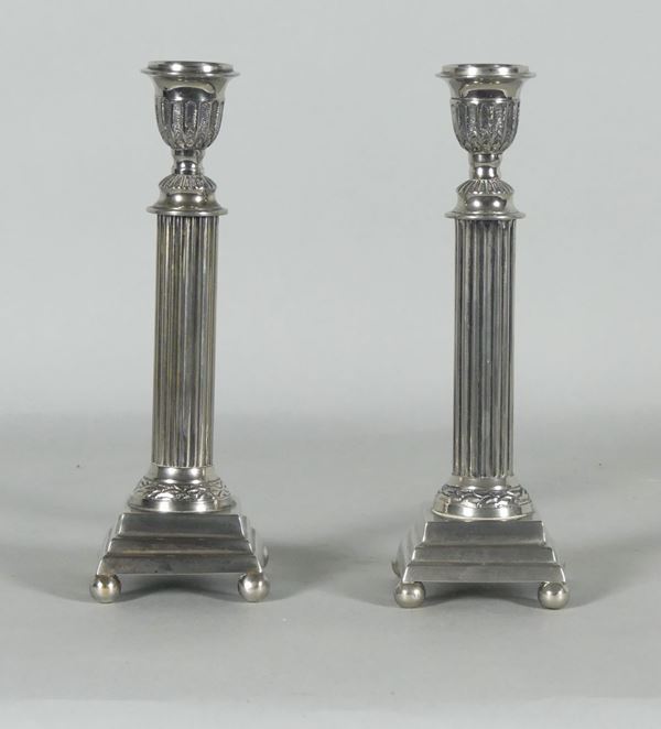 Coppia di candelieri a colonna in metallo argentato e sbalzato