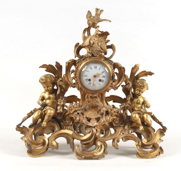 Antique French clock in gilded bronze, chiseled and embossed with sculptures of cherubs, floral garlands and eagles, dial in white enamel with Roman numerals