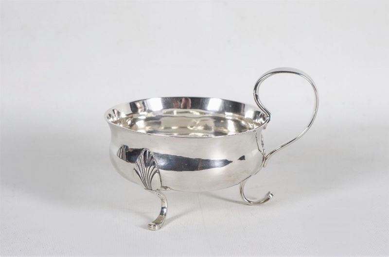 Grande tazza con manico in argento, sorretta da tre piedini ricurvi a motivi Impero, gr. 390