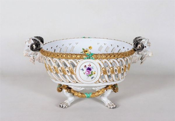 Cesto traforato in porcellana policroma di Meissen, con decorazioni dipinte a mazzetti di fiori  e cordoni in oro zecchino, manici a teste di caproni e quattro piedi leonini