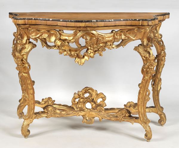 Roman Louis XV console in gilded wood, carved and sculpted, with four legs with wide scrolls enriched with acanthus leaves and flowers, joined by a shaped crosspiece. Undertop with friezes with volutes, triplets and floral motifs, arched top in marble plated in antique yellow veined with upper thread in smooth cordon in antique black marble