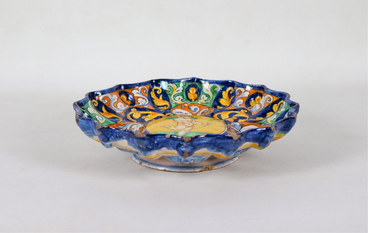 Crespina in maiolica smaltata di Faenza, dipinta e decorata in blu, arancione e giallo con ornati...