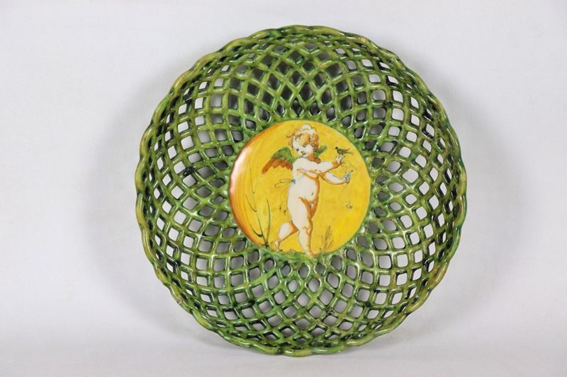 Crespina in maiolica smaltata di Faenza, a forma di cesto traforato, con al centro putto a compen...