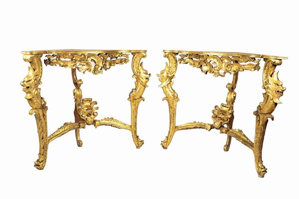 Coppia di angoliere di linea Luigi XV, in legno dorato ed intagliato a motivi di ricci, volute e teste di mascheroni, tre gambe ricurve riunite da crociera sagomata. Mancanti dei piani 