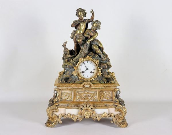 Antique French table clock in gilt bronze and white marble, with sculptures of Putti and dog, supported by shell feet. White enamel dial with Roman numerals