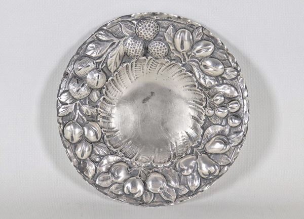 Antico piattino tondo in argento, con bordo cesellato e sbalzato a motivi di frutta, sorretto da tre piedini ricurvi, gr. 140