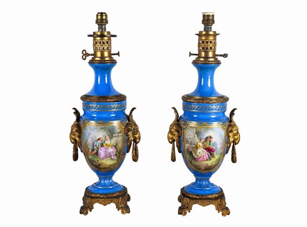 Pair of oil lamps in light blue Sèvres porcelain, with pure gold highlights, painted squares with "Romantic scenes and landscapes", handles in gilded bronze and chiseled with goat heads and bases with acanthus leaves motifs