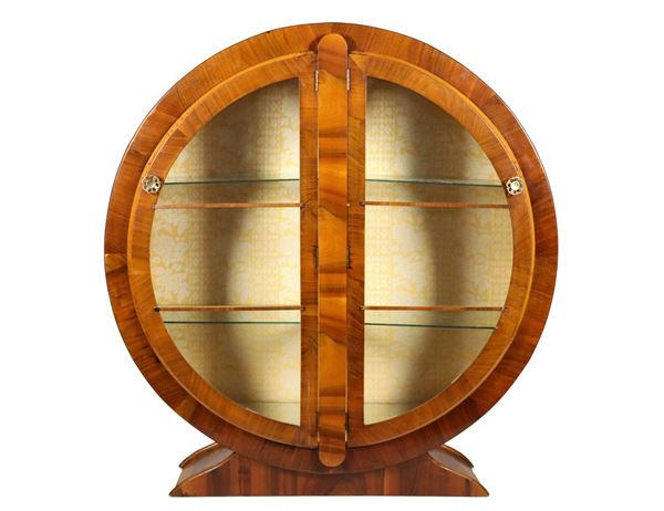 Round-shaped showcase of the Decò line in walnut, with two crescent-shaped doors and glass shelves inside