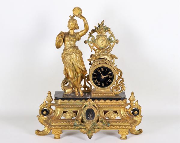 Antique French Louis Philippe table clock, in gilded, embossed and chiselled metal with sculpture of "Odalisque and musical instruments", black enamel dial with golden Roman numerals