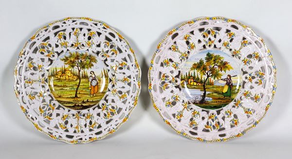 Coppia di piatti da muro in maiolica smaltata e porcellanata di Castelli, con bordi traforati e scene di paesaggi con contadine al centro