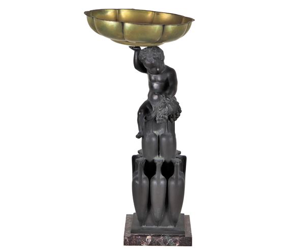 Antico gruppo in bronzo "Putto con leone e anfore", sormontato da coppa in metallo e sorretto da basetta in marmo rosso brecciato