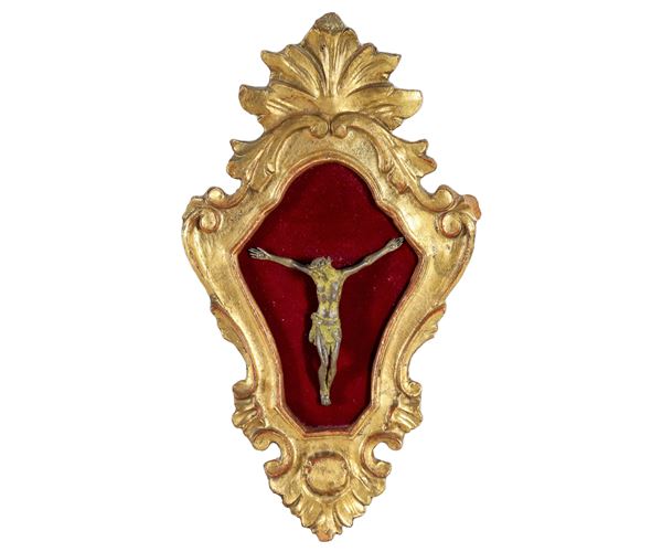 Ancient small bronze crucifix in carved and gilded wooden frame, red velvet background