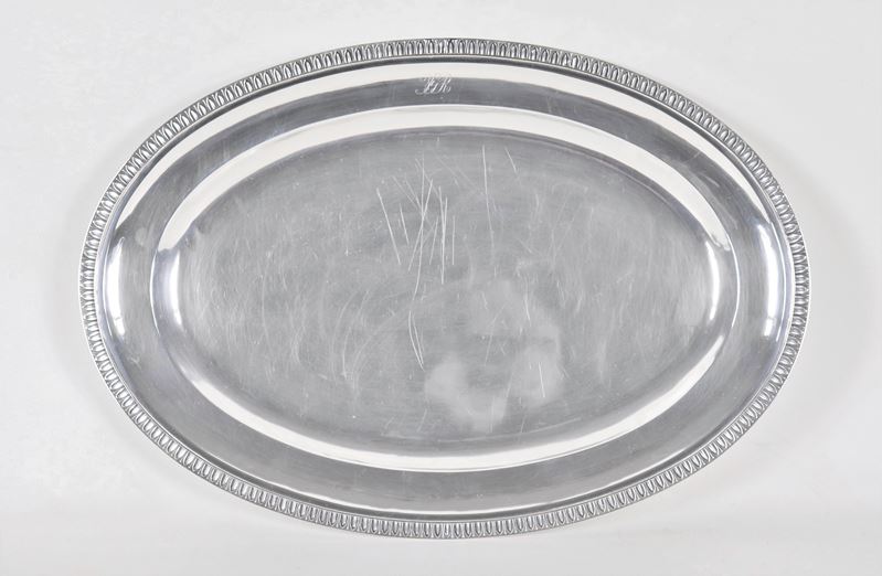 Grande piatto ovale da portata in argento, con bordo cesellato a palmette neoclassiche e monogram...