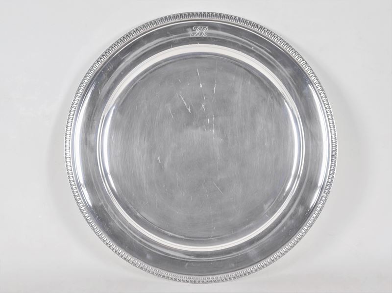 Grande piatto tondo da portata in argento, con bordo cesellato a palmette neoclassiche e monogram...