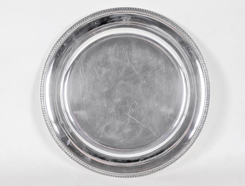 Grande piatto tondo da portata in argento, con bordo cesellato a palmette neoclassiche e monogram...