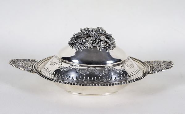 Piccola legumiera in argento a forma ovale, cesellata e sbalzata a motivi Luigi XVI, con manici a forma di conchiglie e pomo con sculturina di agnellino, ghiande e fiori, gr. 780