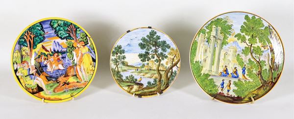 Lotto di tre piccoli piatti in maiolica italiana lustrata e variopinta, con scene di paesaggi e scena mitologica