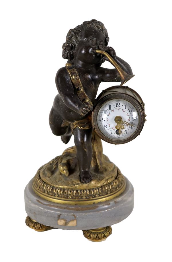Piccolo orologio da tavolo sorretto da scultura in bronzo di "Putto suonatore", quadrante in smalto bianco e base in marmo