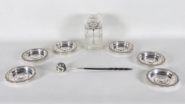 Lot of a worked crystal bottle with silver neck and spoon, six silver-plated coasters and a small silver-plated ladle with a George III coin in the center (8 pcs)
