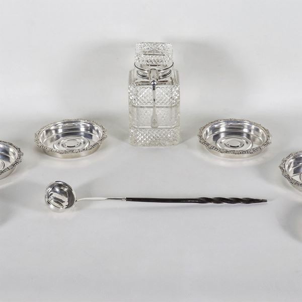 Lot of a worked crystal bottle with silver neck and spoon, six silver-plated coasters and a small silver-plated ladle with a George III coin in the center (8 pcs)