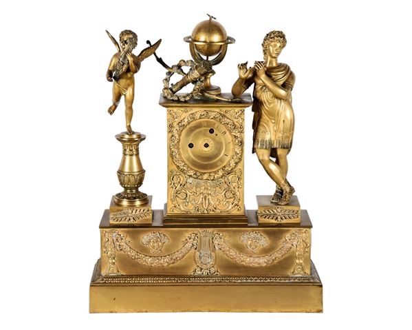Empire Period French table clock in gilded bronze, embossed and chiselled with motifs of garlands, lyre and Meduse's heads, globe in the center and arch with quiver, sculptures of Apollo and Putto with lyre on the sides