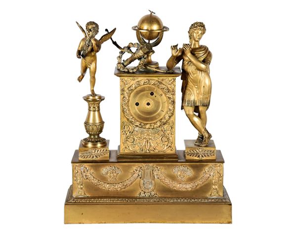 Pendola da tavolo francese Epoca Impero in bronzo dorato, sbalzato e cesellato a motivi di ghirlande, lira e teste di Meduse, al centro mappamondo e arco con faretra, ai lati sculture di Apollo e Putto con lira