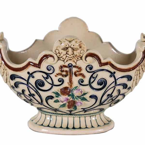 Small oval-shaped centerpiece in porcelain ceramic, with colorful decorations in relief with motifs of scrolls and fruit, handles in the shape of eagle heads