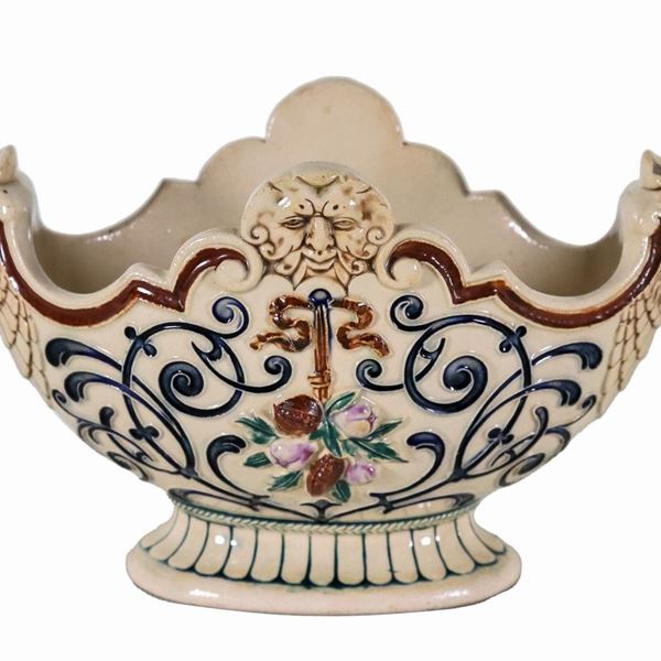 Piccolo centrotavola in ceramica porcellanata a forma ovale sagomata, con decorazioni variopinte a rilievo a motivi di volute e frutta, manici a forma di teste di aquila